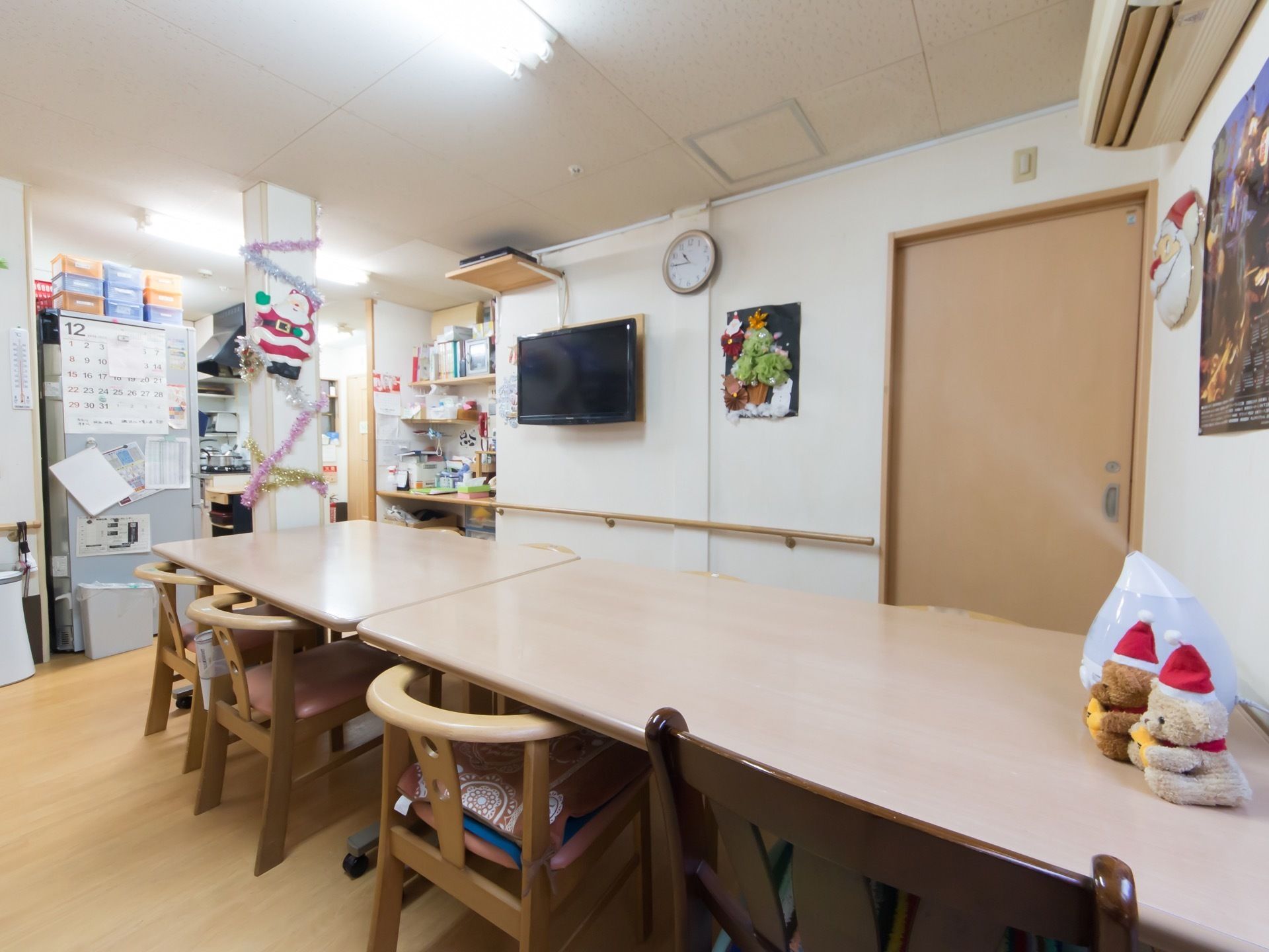 中央に木製のテーブルセットが置かれている。周囲に１人用の椅子がたくさん並べられている。左奥に冷蔵庫がある。