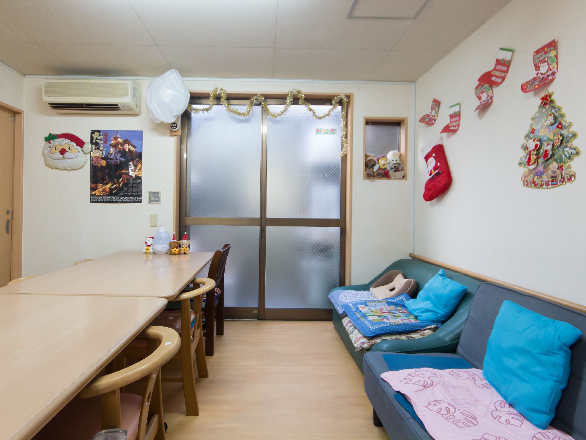 壁にクリスマスの飾り付けがあり、ソファとダイニングテーブル、椅子が設置された部屋