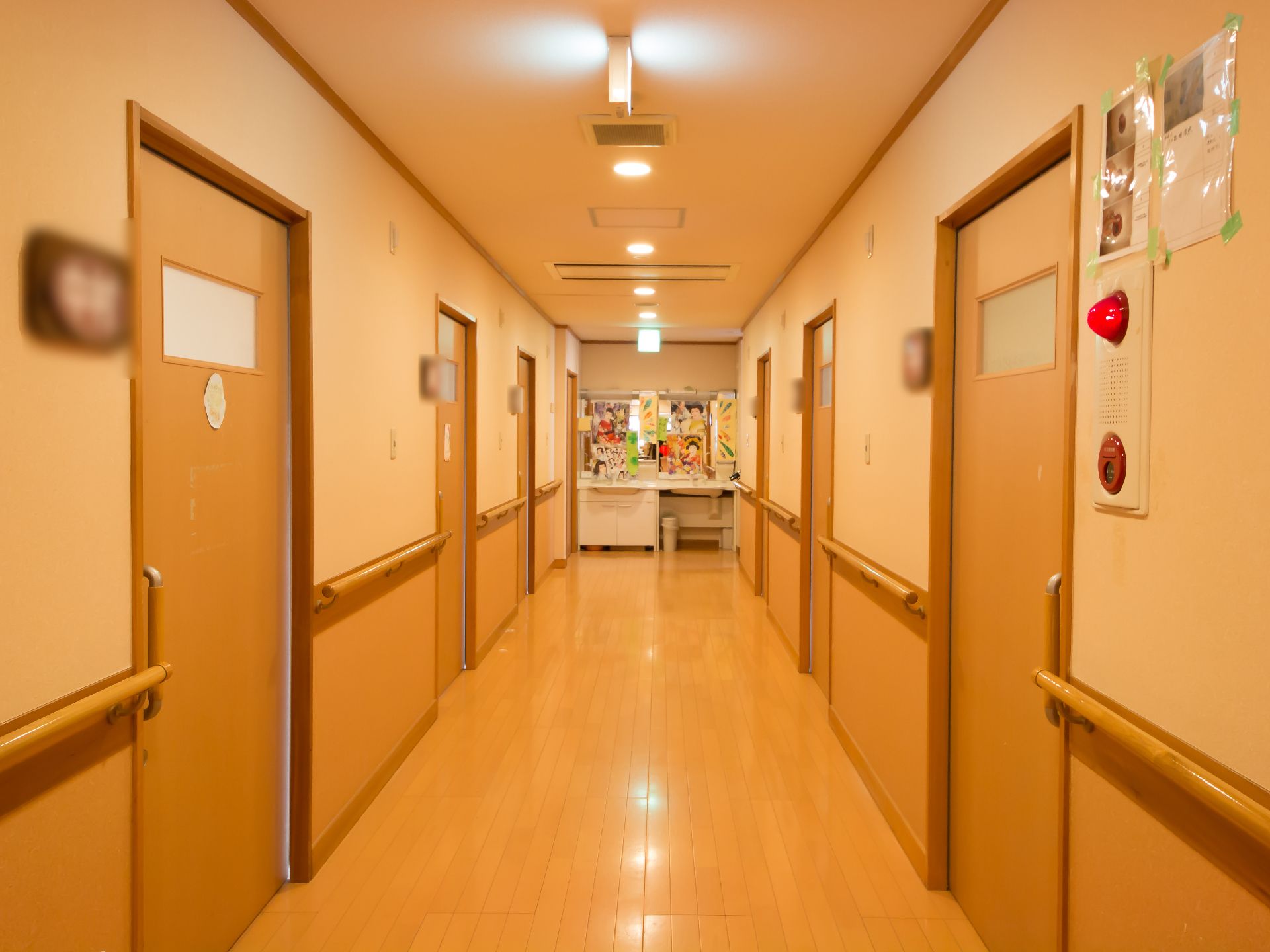 フローリングの廊下で、両側に居室へのドアが等間隔で並んでいる。壁には消防設備のサイレンが取りつけられている。