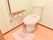 トイレは水洗トイレ。便座カバーと足置き、スリッパあり。壁には手すりとトイレットペーパーが設置されている。呼び出しスイッチもあり。