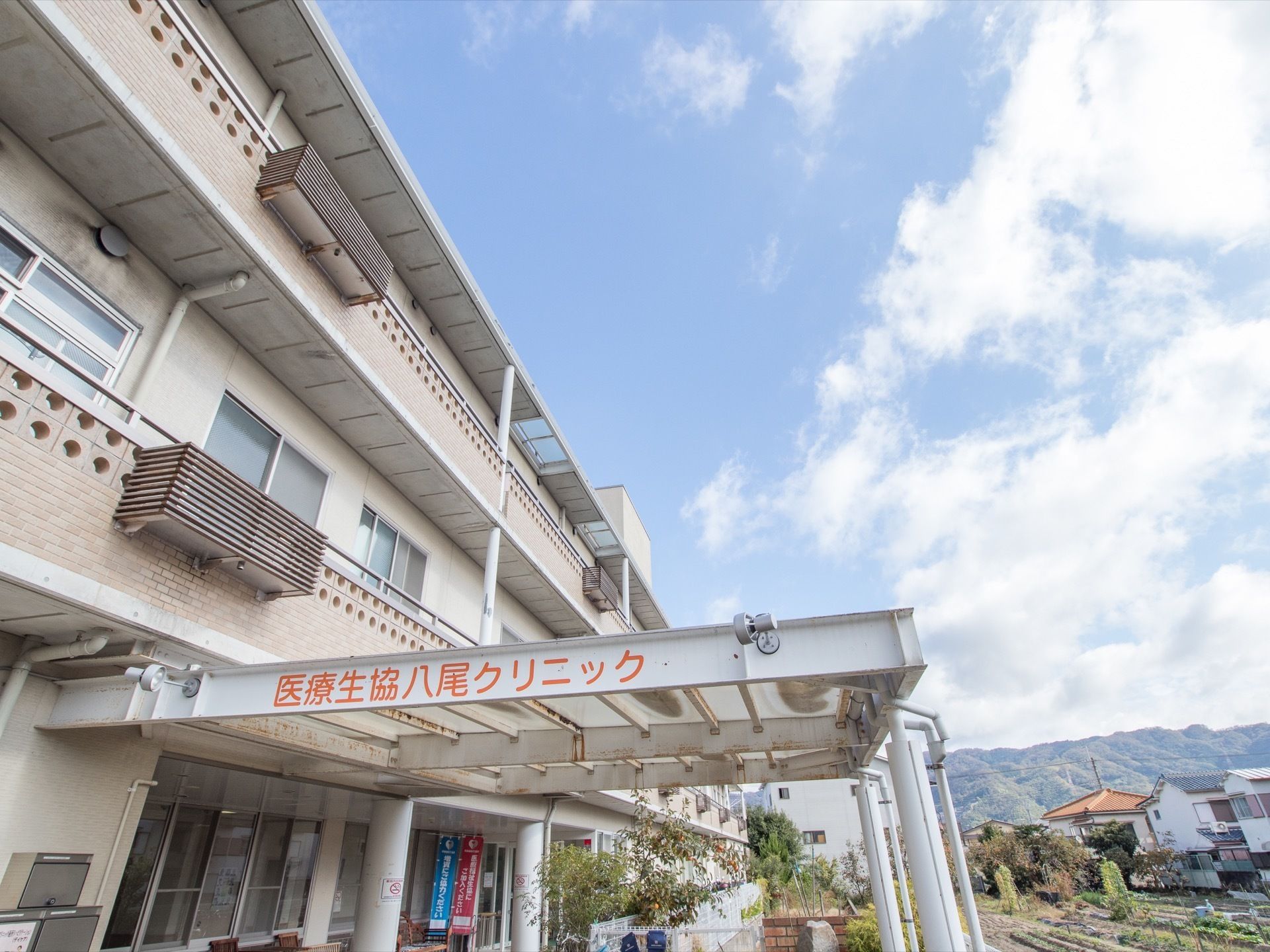 コンクリート３階建ての建造物である。目の前には畑が広がっている。玄関の上には大きな屋根が設置されている。