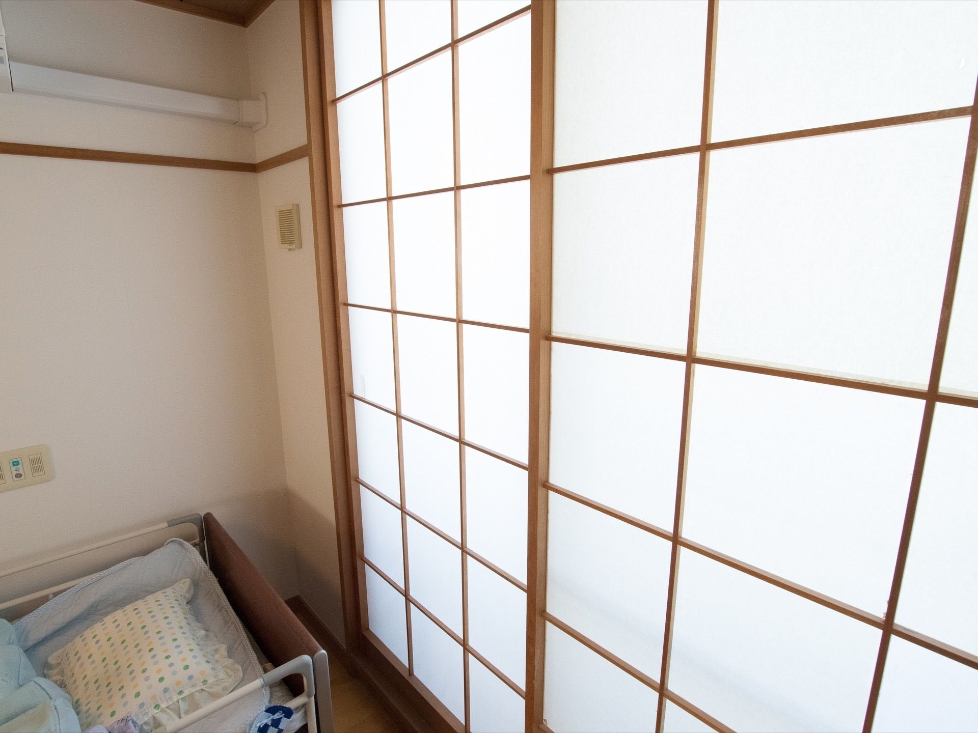 居室の一部分である。掃き出し窓には、障子がある。部屋の雰囲気と木枠がマッチしている。障子を頭側にしたベッドも置かれている。