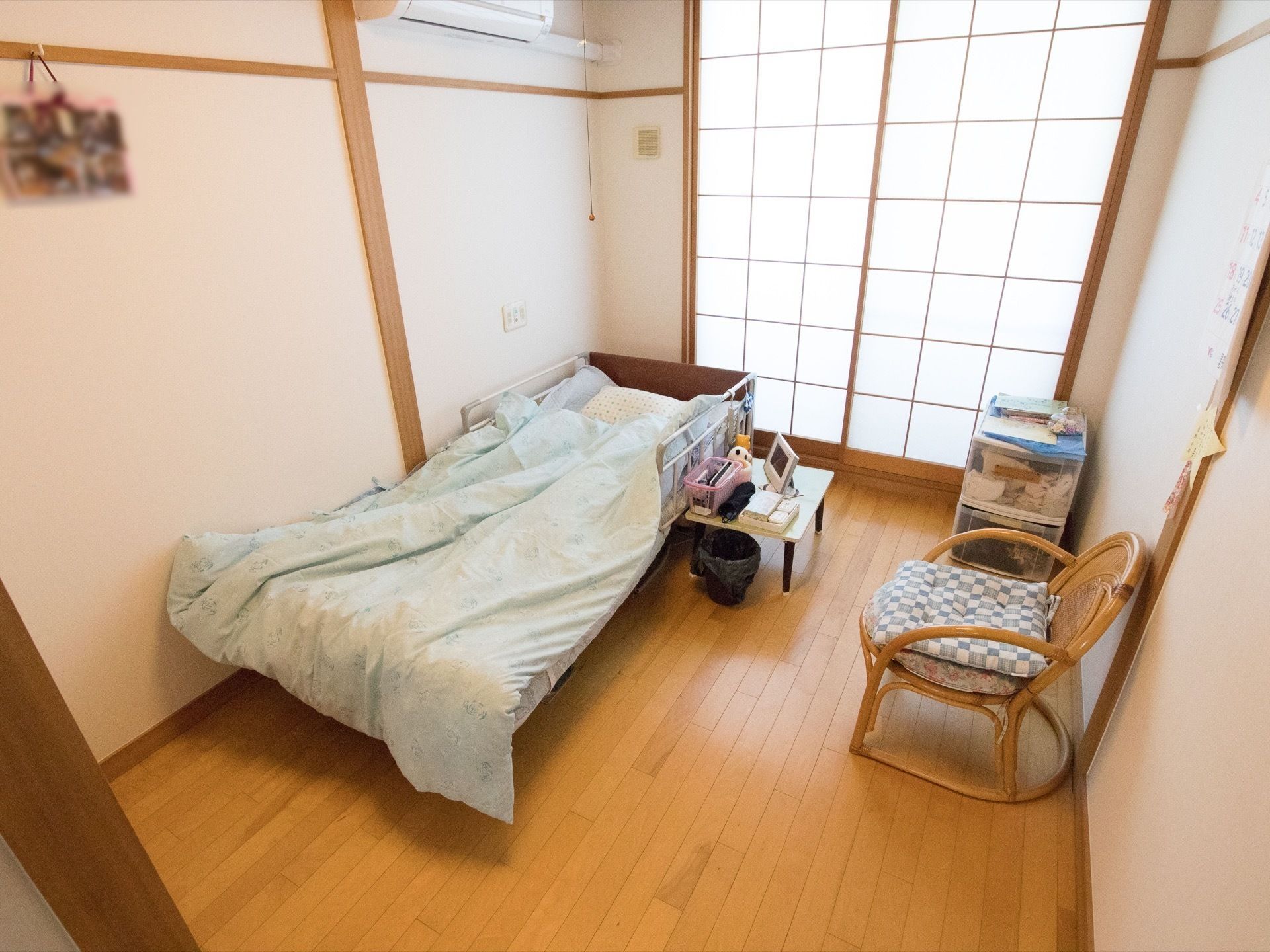 ベッドの布団の中に入り微笑む高齢の女性と、女性の手を取り語り掛けるエプロン姿のスタッフ。