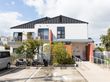 ２階建ての建物がある。玄関先には大きな植え込みがあり、手すりとスロープが続いている。正面には駐車場がある。