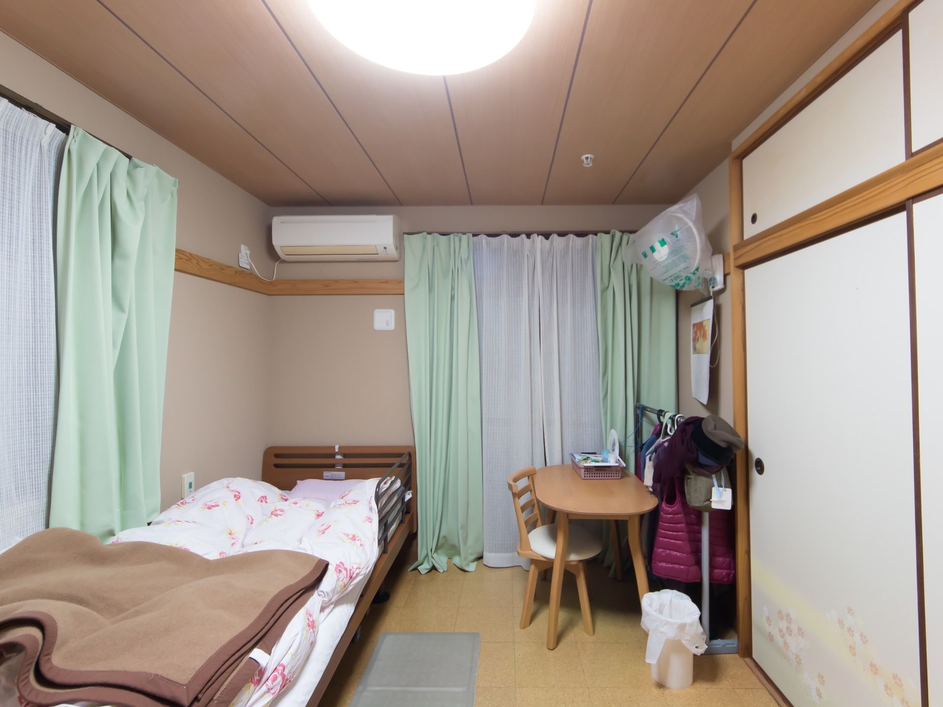 押入れや袋戸棚が設えられた和室仕様の居室である。エアコンが設置され、フローリングに介護用ベッドが置かれている。
