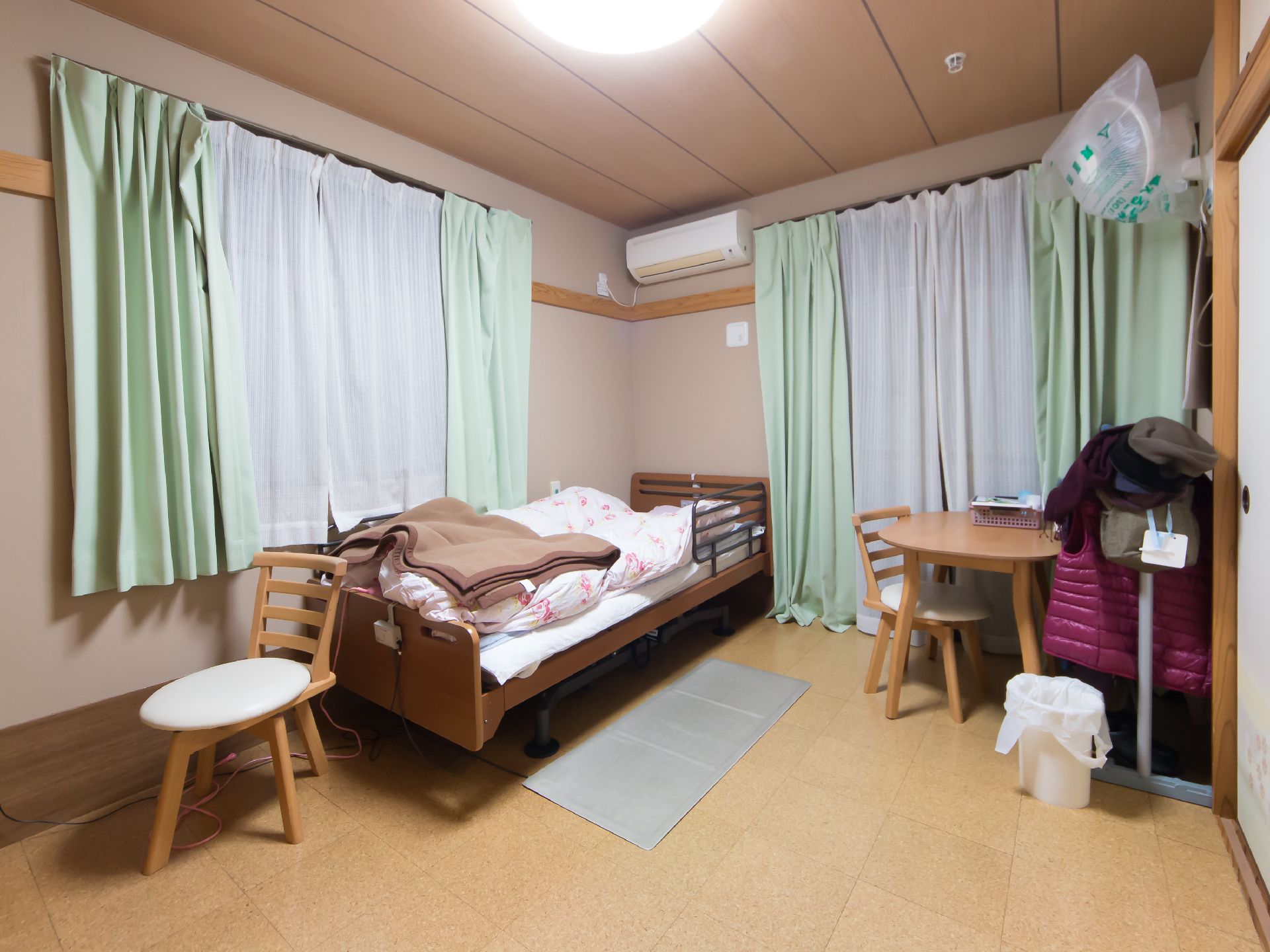 介護用ベッドとテーブル、イスが置かれていて、窓が二つある部屋