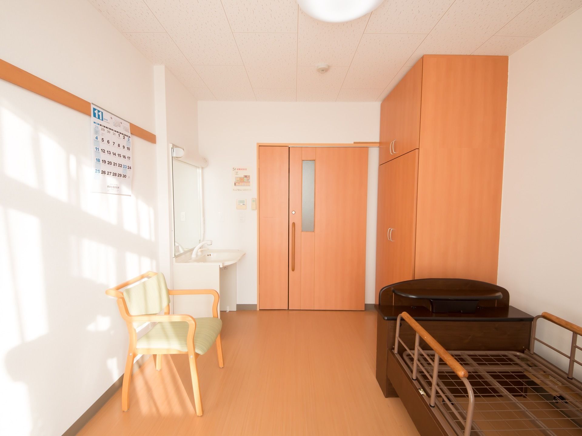 広い個室になっている。室内には、大きな収納棚や介護用ベッドだけではなく、椅子や洗面台も設置されている。