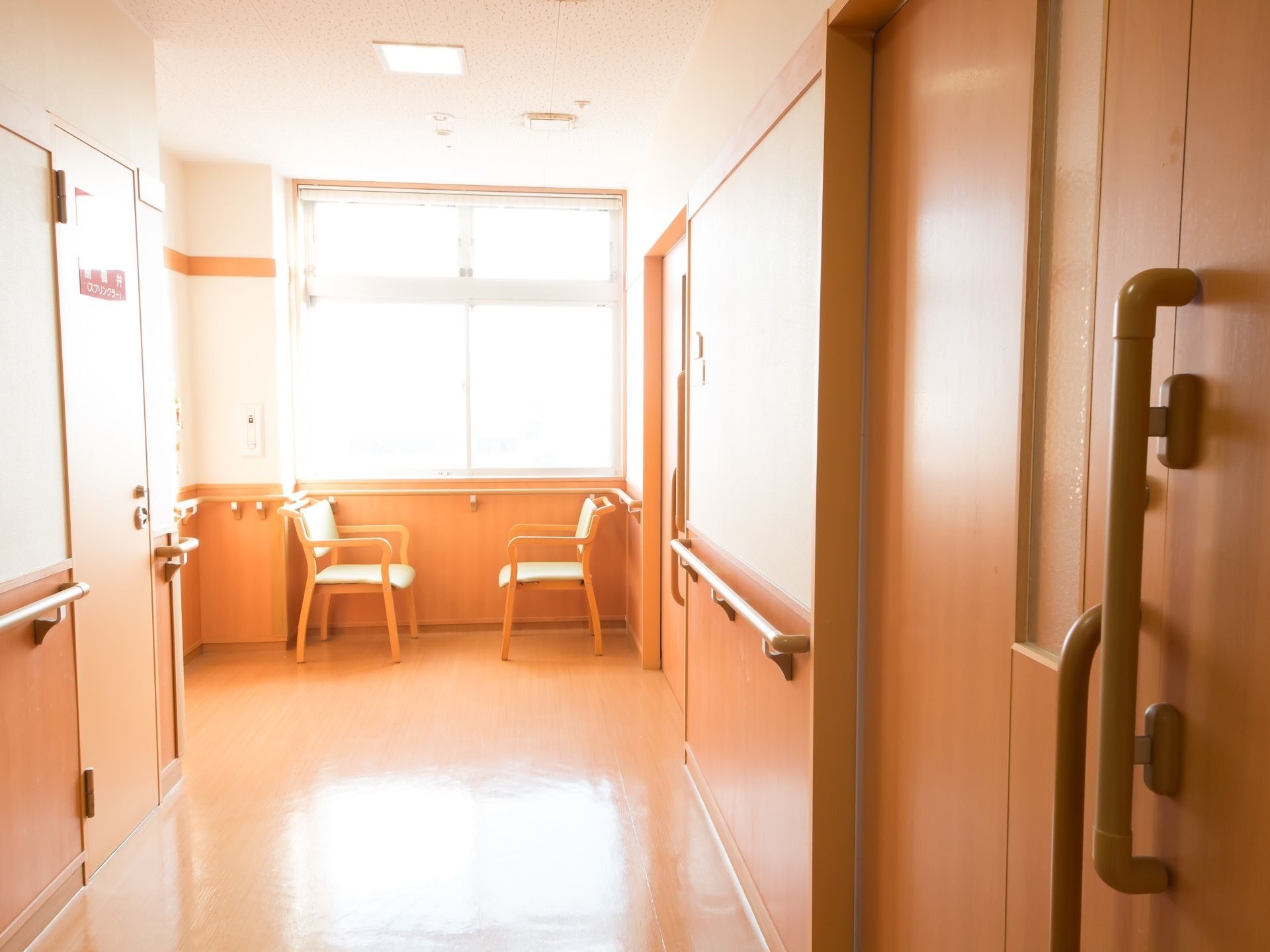 廊下の窓からあたたかい日差しが差し込んでいる。窓際に椅子が向かい合うように並べられており、壁には手すりがついている。