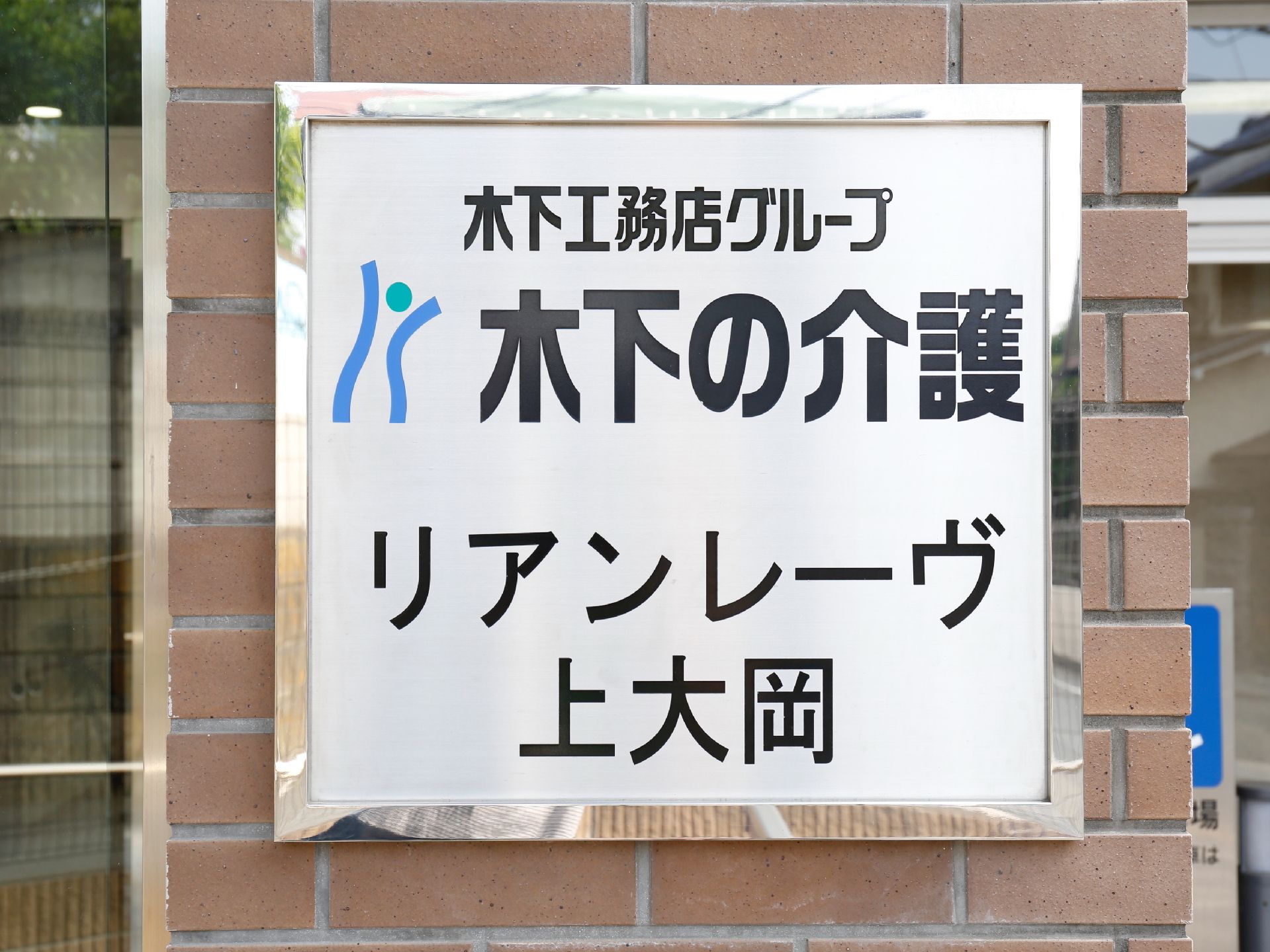 レンガ調の壁に金属のふちで白のパネルに黒の文字で施設名とロゴが大きく書かれている。文字も大きく判りやすいデザイン。