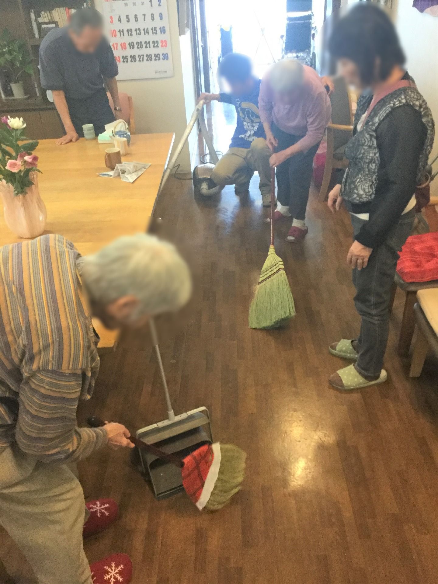 入居者とスタッフがともに床にほうきをかけている。