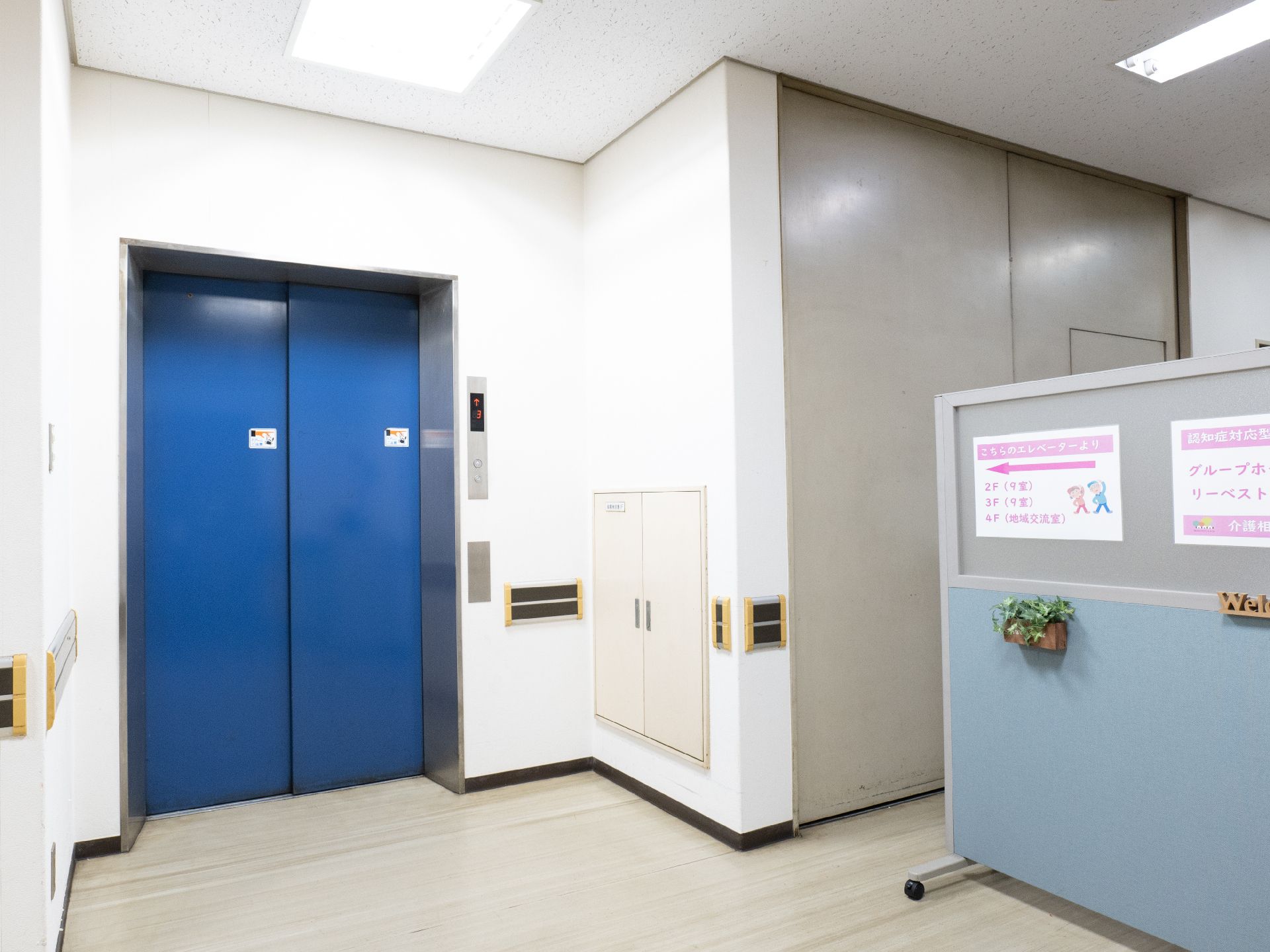 こちらを向いて笑顔になる車いすの高齢女性と介護施設の女性スタッフの様子