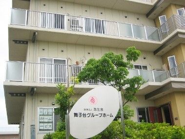 各フロアにベランダが付いた3階建ての建物の周りには木が植えられ、館銘板もある。