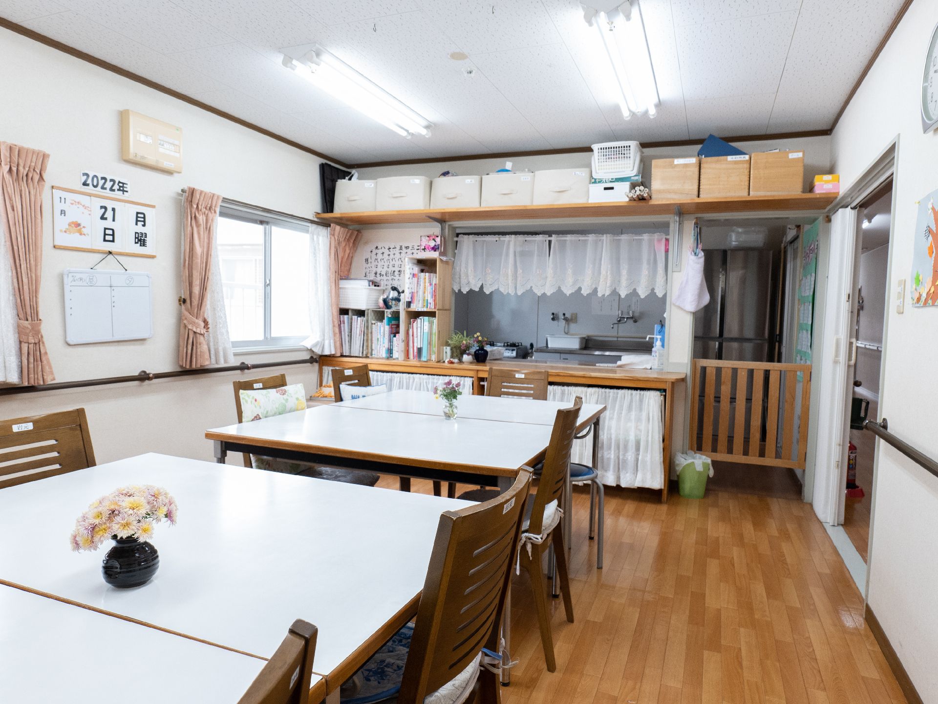 水の入ったコップを持って微笑むエプロンを付けた女性スタッフと薬を飲もうとしている高齢女性がいる。