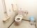 薄いピンクのトイレにはふたがなく、両サイドには手すりがあり、呼び出しボタンも壁に付いている。