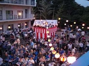 敷地内には多くの人があふれ活気がある納涼祭の様子。薄暗くなってきた中、提灯の明かりが映える。