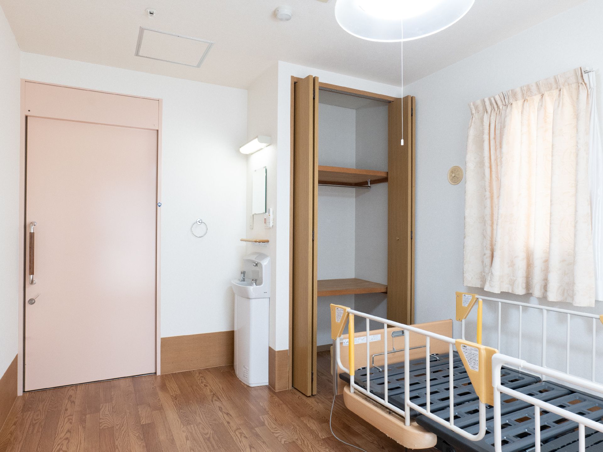 カーテンが付いた大きな窓がありベッドが置かれている居室