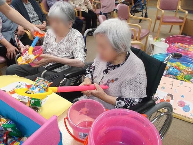 室内で行われている祭りの様子。スコップでおやつをすくったり、ヨーヨー釣りをしたりして楽しんでいる高齢者たち。
