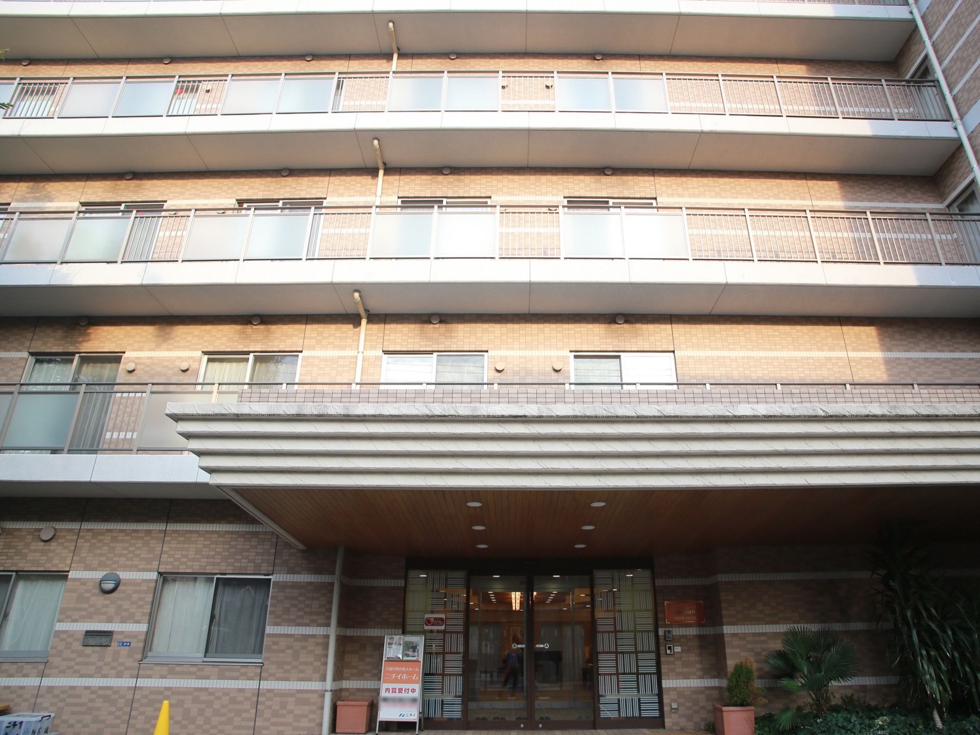 玄関前には大きな屋根が掛けられている。２階以上には、ベランダと窓が連続していて、陽光が当たっている。