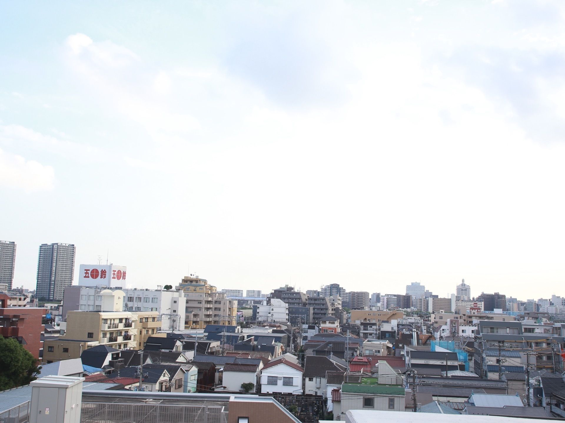 手前には階数の少ない建物が隙間なく並んでいる。遠くに商業ビルやマンションなど高層の建物が数多く建っている。