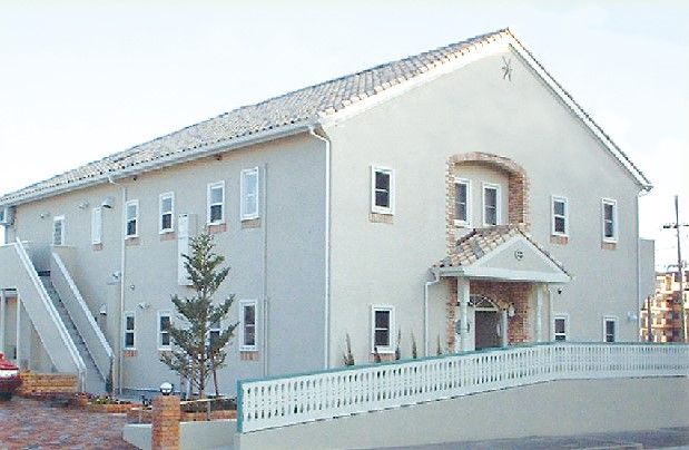 パジャマ姿でベッドに横になっている高齢女性に温かく介護に当たるエプロン姿の女性スタッフ。