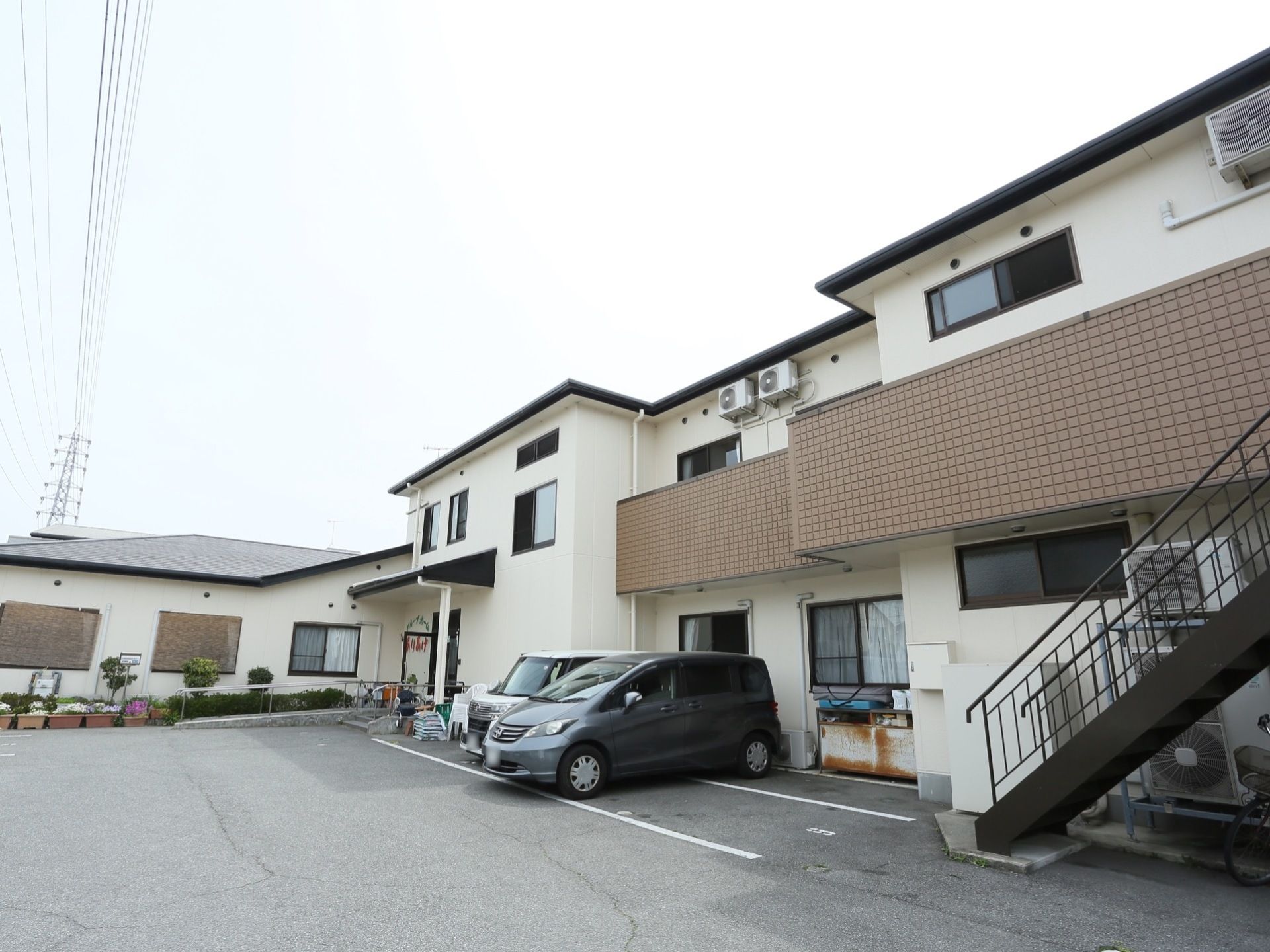 白く明るい外装の建物が広々とした敷地にゆったりと建てられている。エントランスのそばに駐車スペースのある機能的なデザインである。