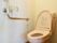 ステンレス仕様のＬ字形手すりが備えつけられたトイレである。淡いピンク色の洋式便座を完備。ナースコールも設置している。