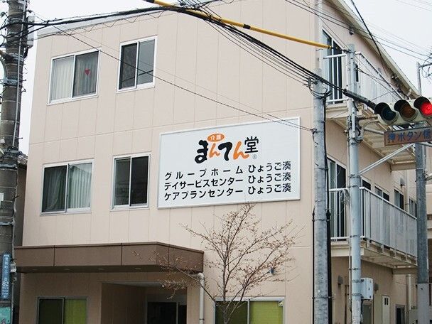 ３つの事業所が一つの建物にあり、それぞれの名前が外壁に書かれている。3階建てでベージュでまとめられている。