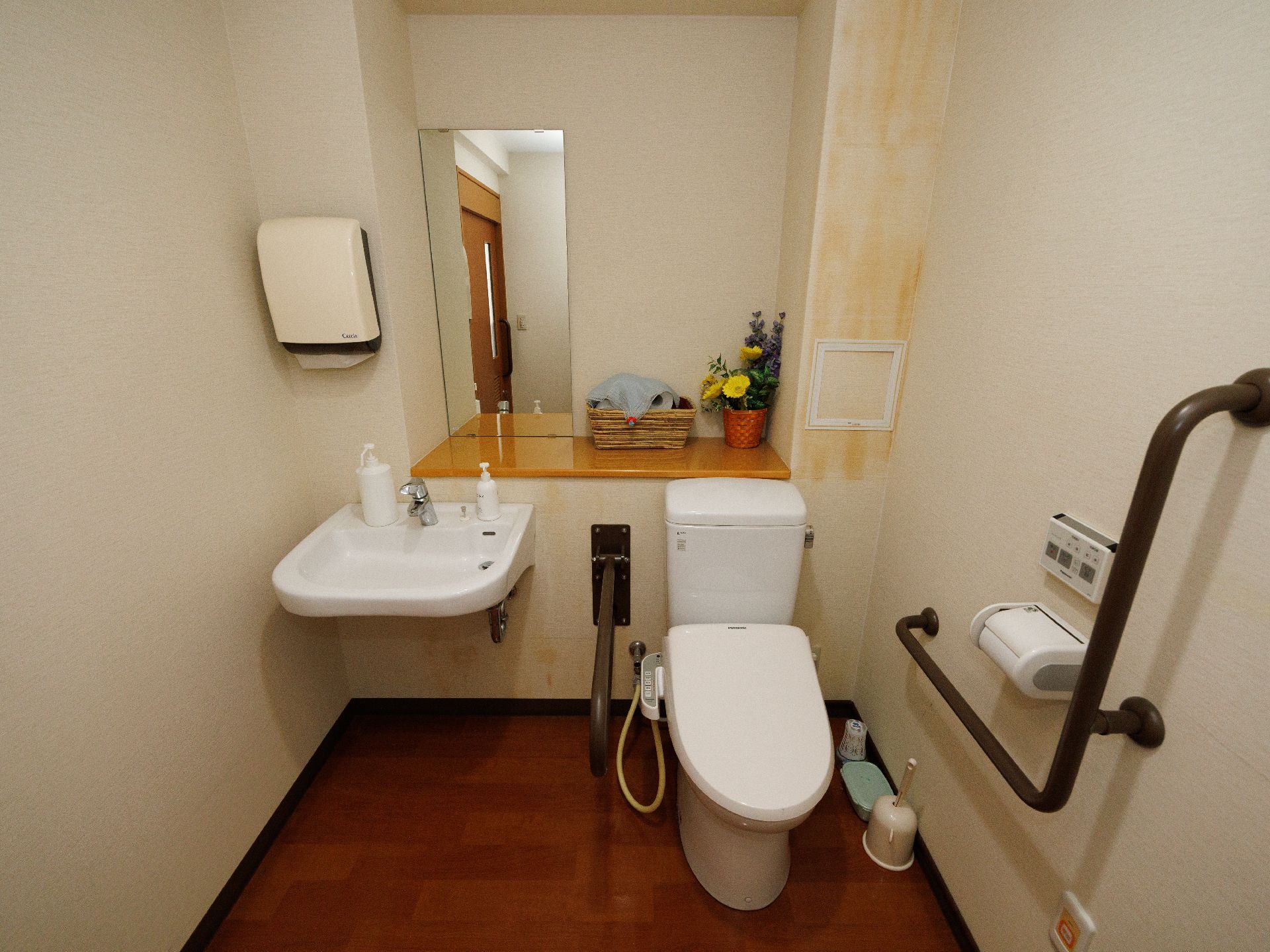 黒い手すりに囲まれた洋式便器と洗面台が並んだ白い壁の部屋