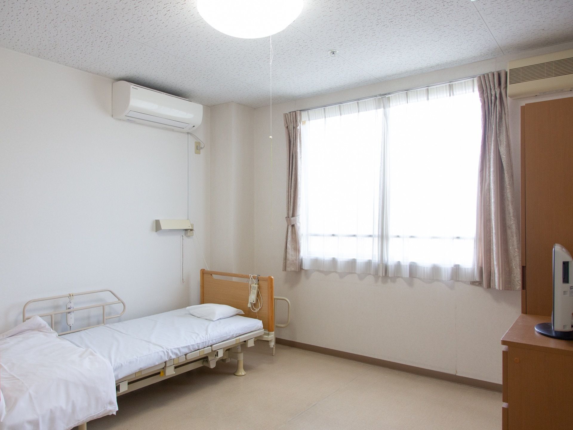 居室には介護用ベットがある。高さが調節できるので、入居者様の好みの高さにできる。窓からは陽が良く差し込んでいる。