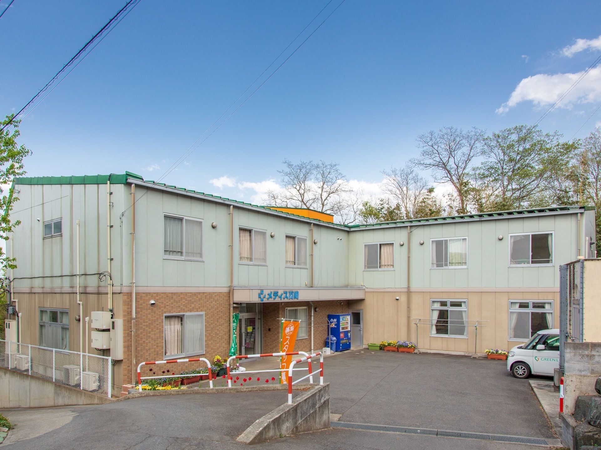 L字型の施設は2階建てで、シンプルな外観である。施設前には車が数台置ける広いスペースがあり、来訪者様も利用できる。