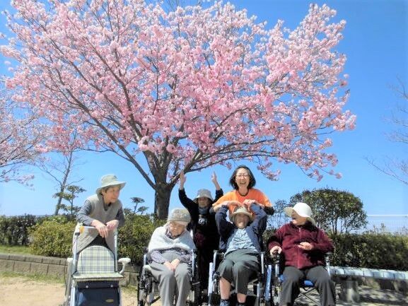 桜の木の下で記念撮影をしている、車椅子や押し車の入居者とスタッフ