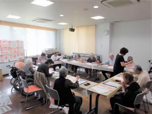 みんなで集まって机に向かい、書道に熱心に取り組んでいる入居者たち