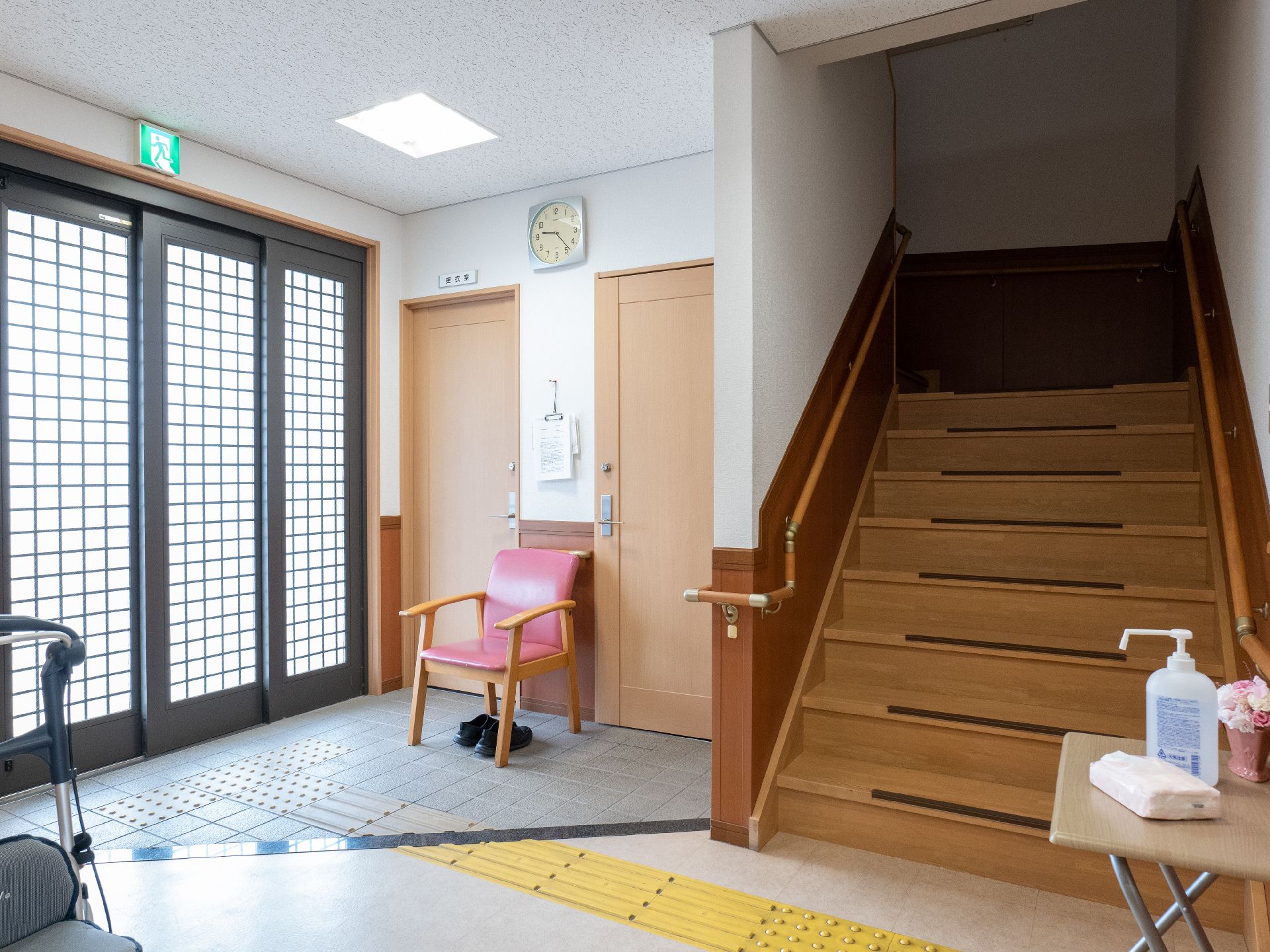 日当たりのいい屋内で笑顔で話している車いすの高齢女性とピンクのエプロンを付けた若い女性スタッフ。