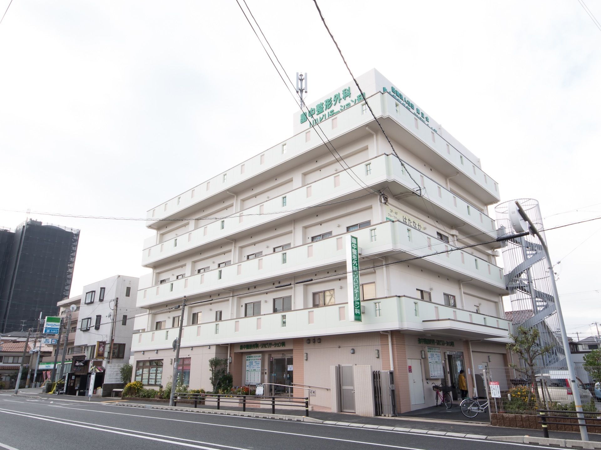 大きな道路沿いに４階建ての病院があり、その中の施設の一つとしてグループホームが入っている。エントランスのそばに駐車スペースがある。