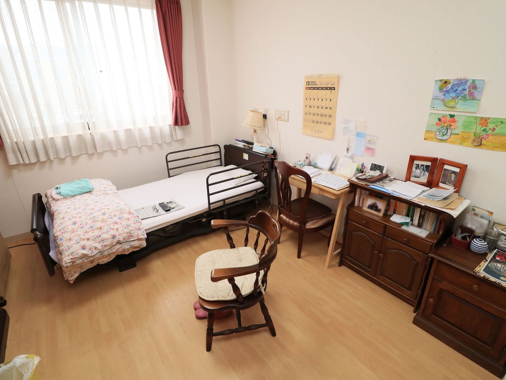 介護用ベッドや机、椅子、棚などが揃った過ごしやすい居室である。壁には入居者様が描いた絵などが飾られている。