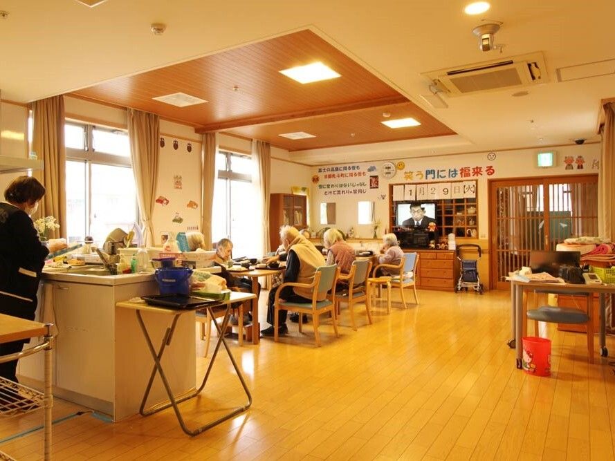 対面式キッチンでスタッフが作業していて、入居者たちはリビングダイニングで食事をしている。