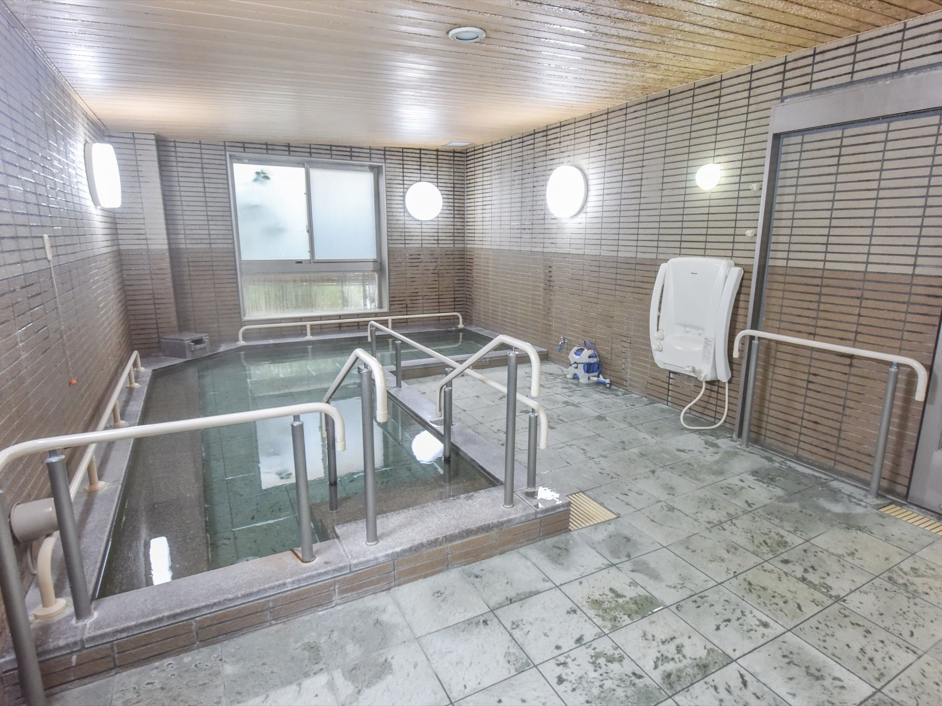 温泉旅館にあるような大きな浴槽の出入り口には、階段と手すりが設置されている。左側の壁には、長い紐の付いた呼出ボタンがある。