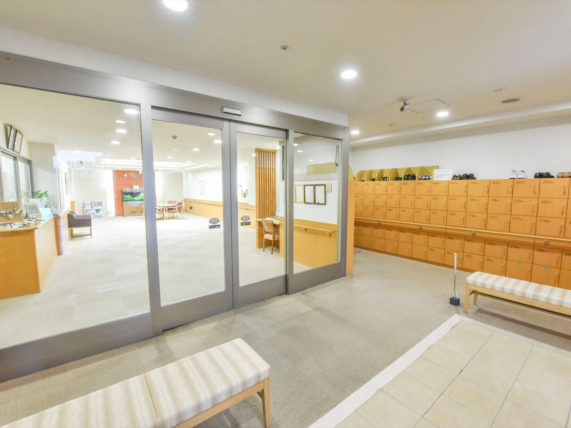 ライトブラウンの靴箱が、壁一面に取り付けられている。靴箱の上にも、スニーカーなどが置いてある。ストライプ模様の長椅子もある。