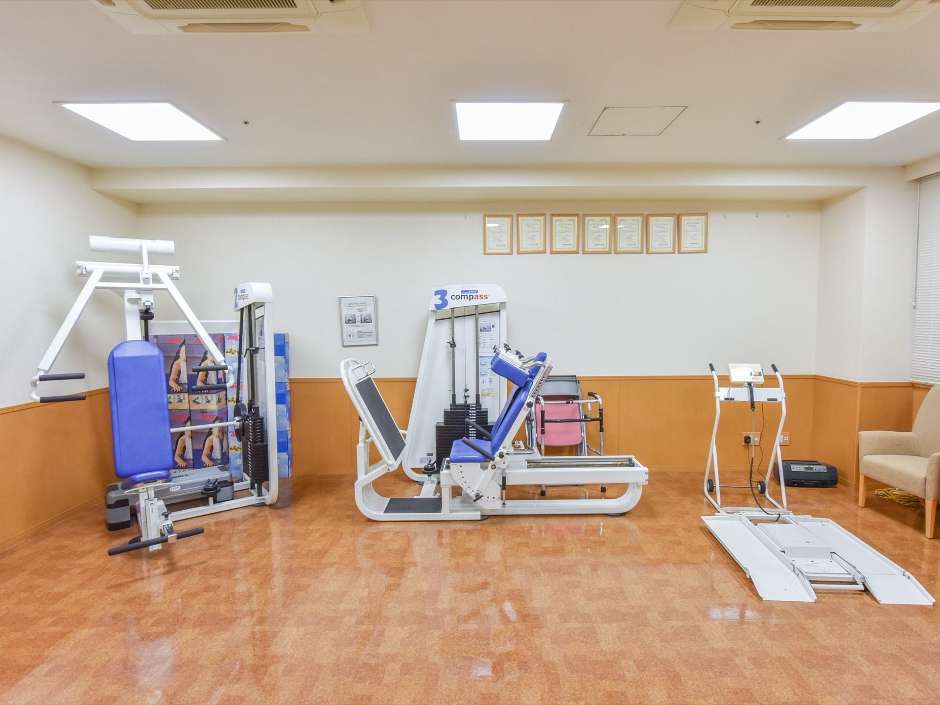 チェストプレス、レッグプレス等、色々な部位を鍛えるマシンが置いてある。右端には、ベージュ色の一人掛け用のソファーがある。