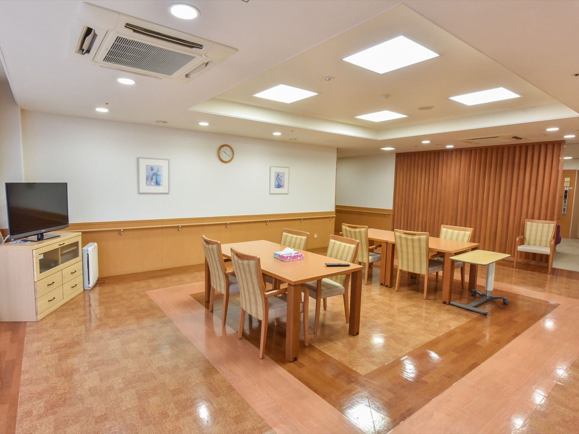 四角や丸い形の照明器具が、天井全体にたくさん取り付けられている。白い壁の真ん中には時計があり、その左右には絵が飾ってある。