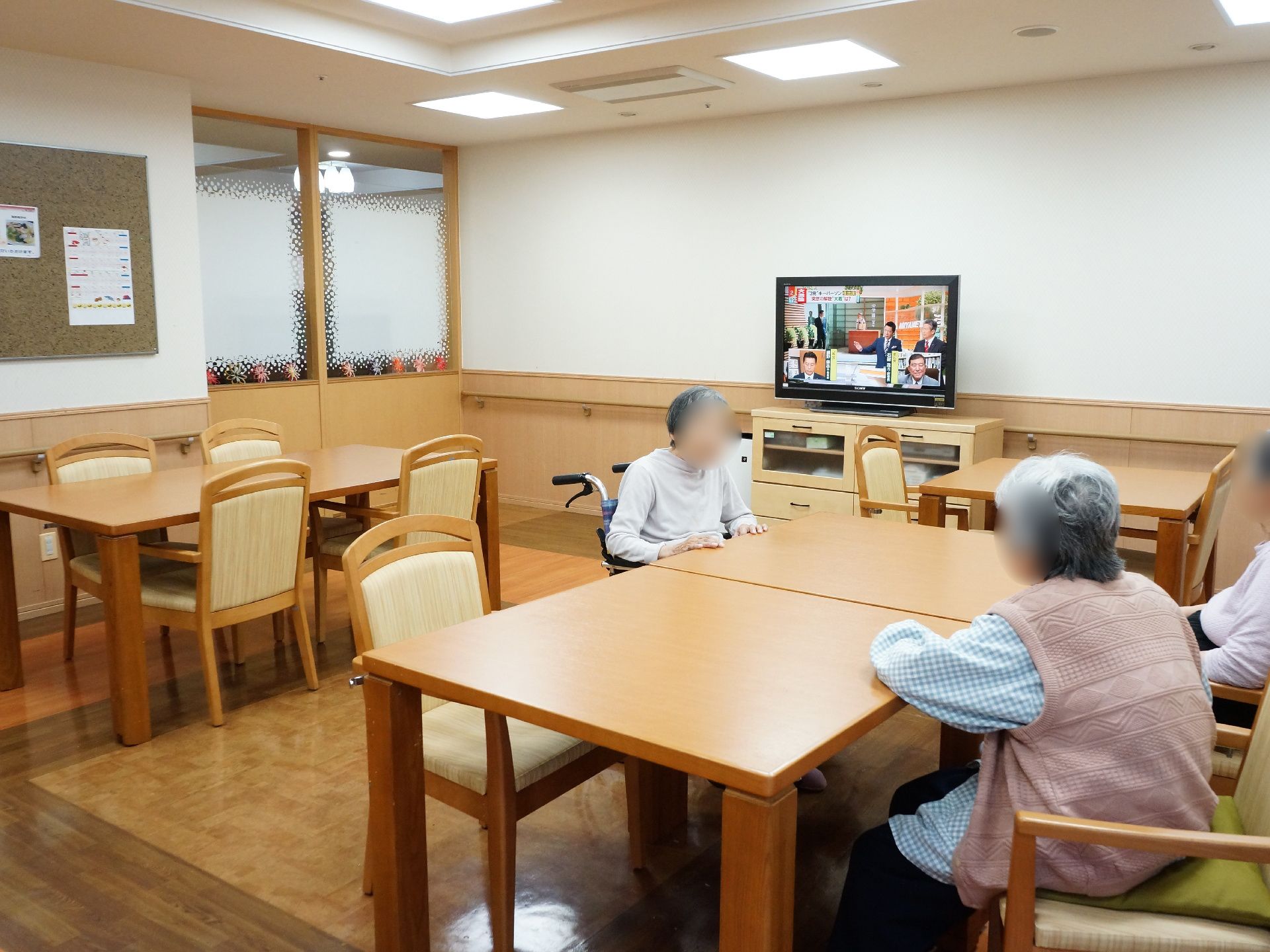 ベージュを基調としたすっきりと整頓されている共有フロアで入居者様たちがテレビを見たり、談笑したりしている。