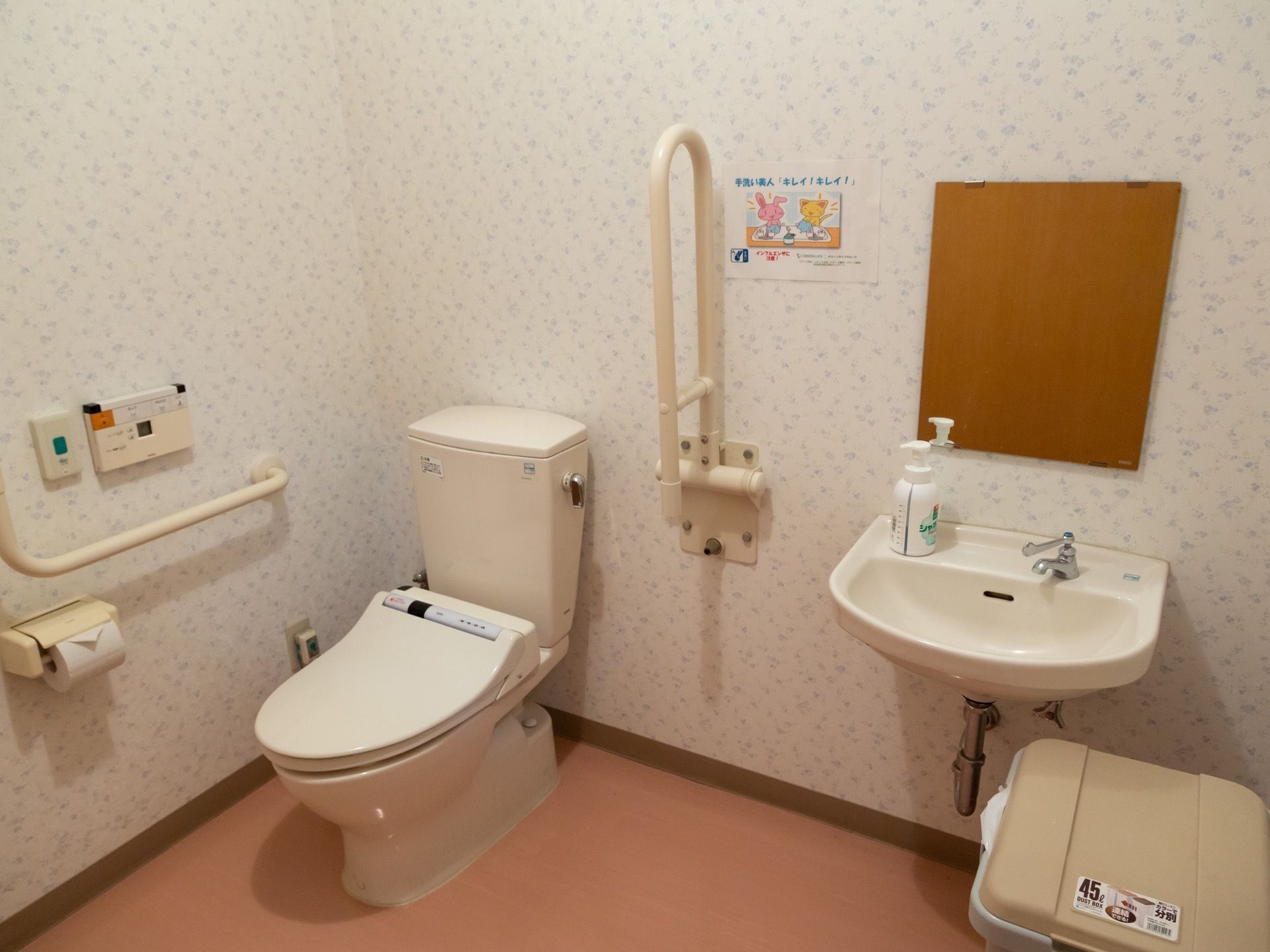 温水洗浄便座機能つきのトイレと洗面台が設置されている。壁には手すりと緊急コールが取りつけられている。