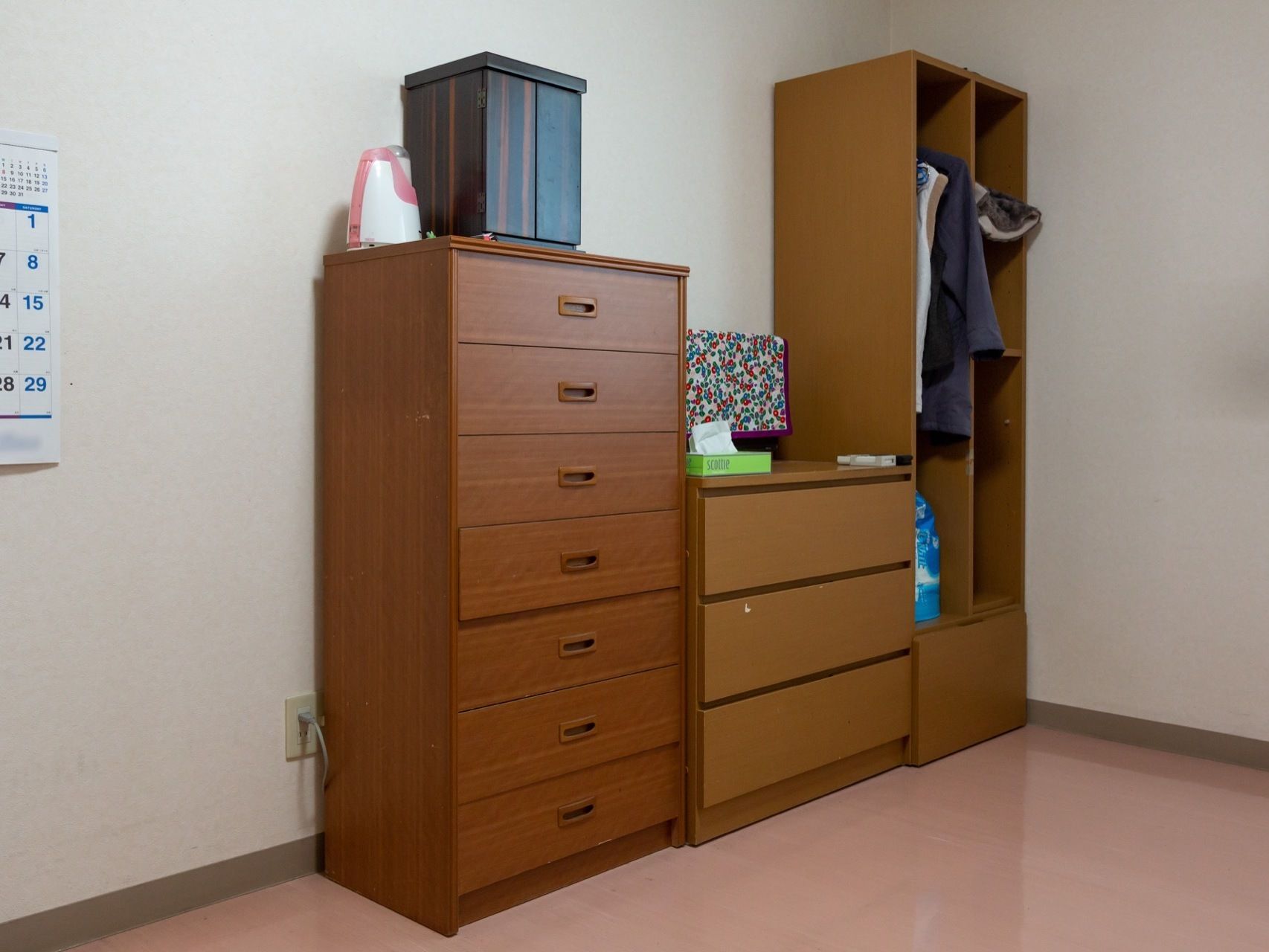 木目調の収納家具が３つ壁際に並んでいる。１つはクローゼット型で洋服がかけられており、２つは高さの違う引き出し型となっている。