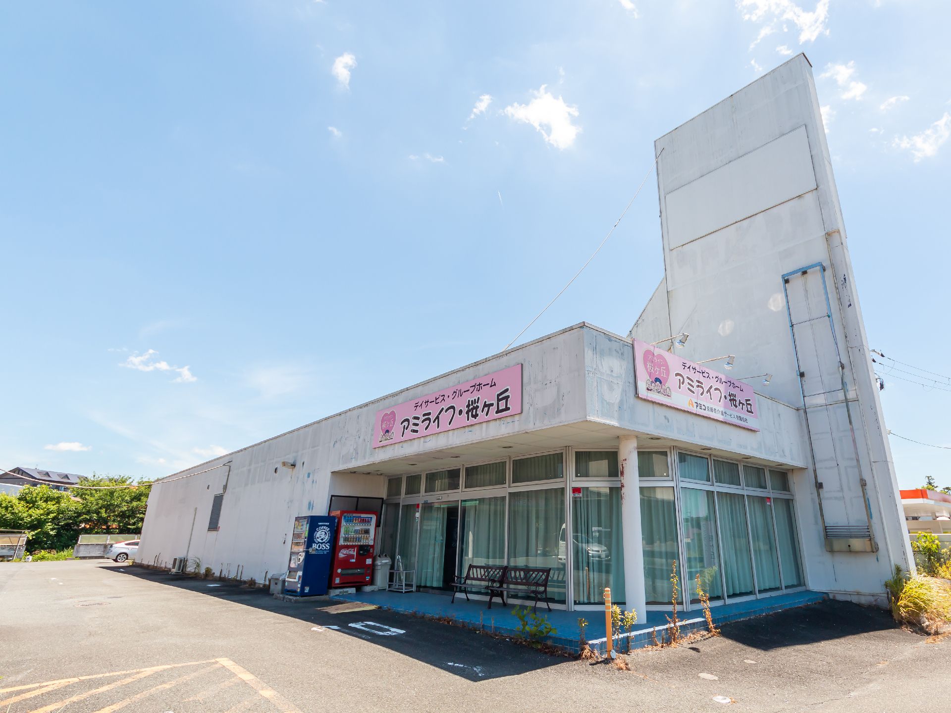 日当たりのいい屋外で散歩を楽しんでいる車いすの高齢女性と付き添いのピンクのエプロンを付けた若い女性スタッフ。