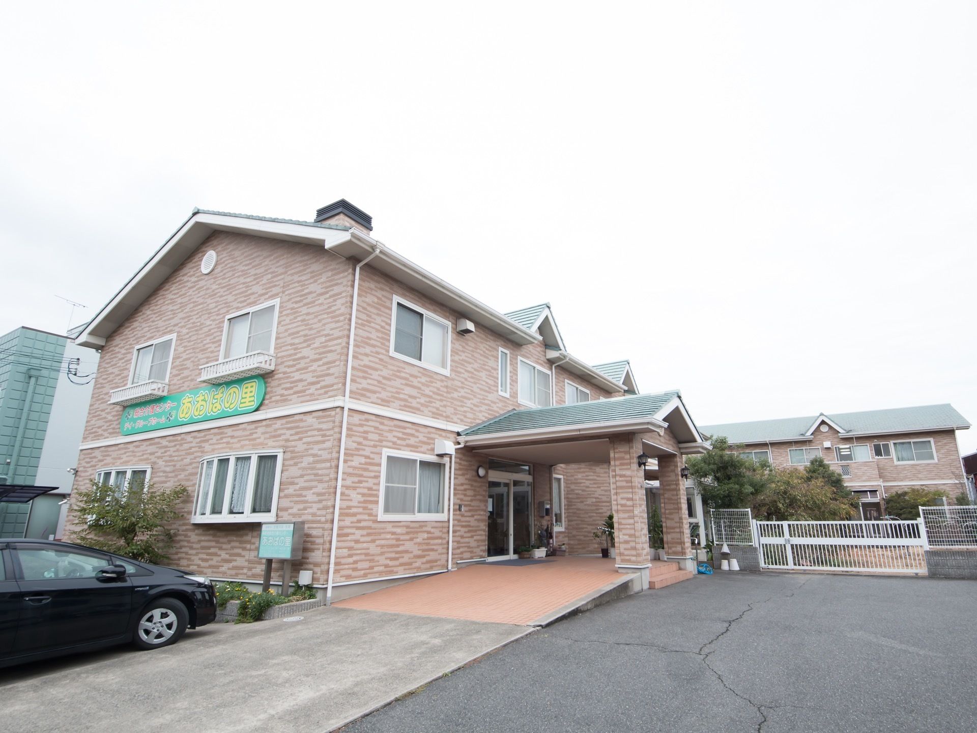 緑色の屋根で壁がブラウン色の2階建の施設になっている。建物の隣に駐車場が設けられており、地面も綺麗に整備されている。
