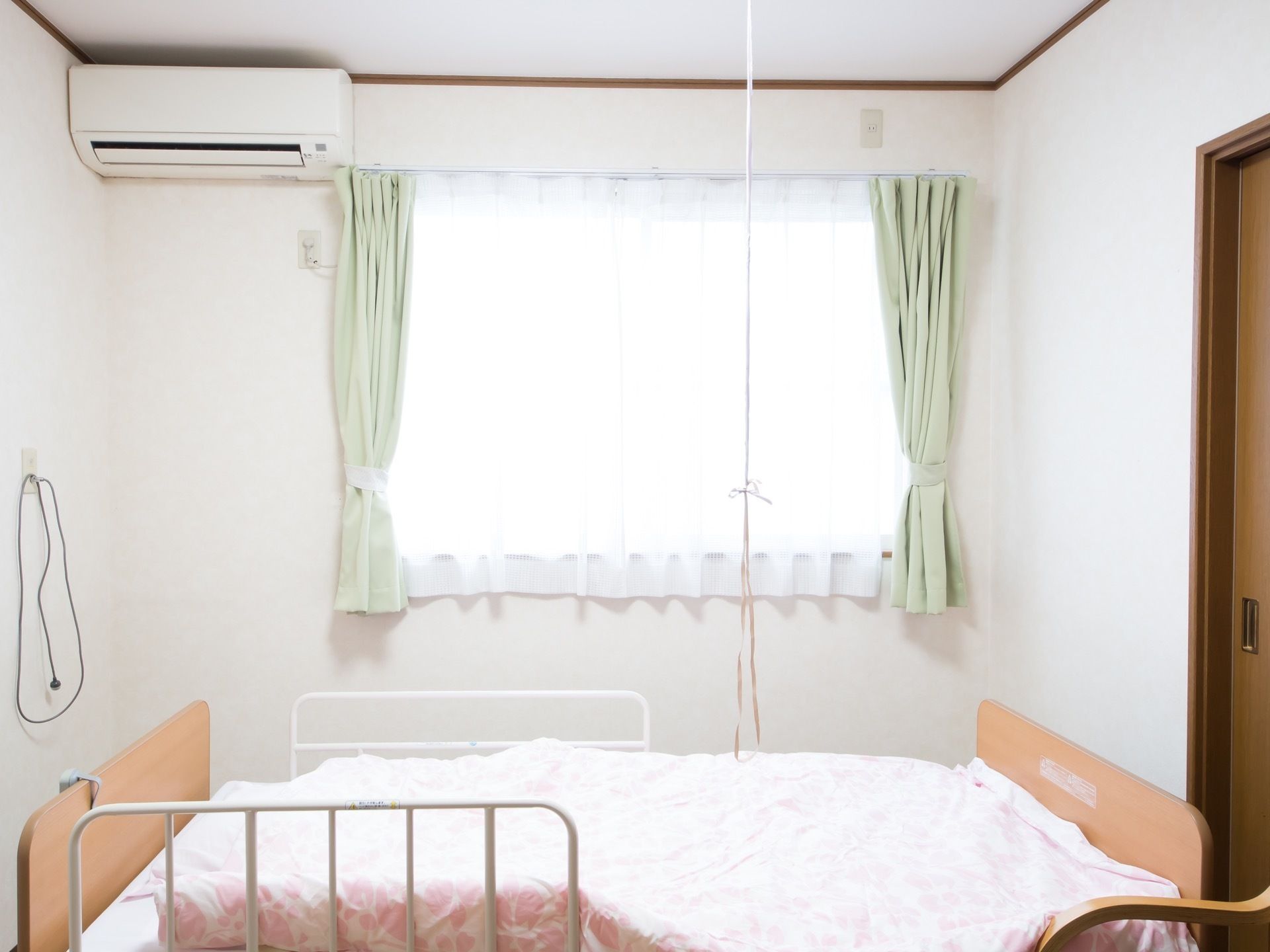 窓からあたたかい日差しが差し込む個室になっている。介護用ベッドが置かれており、壁にはナースコールが設置されている。