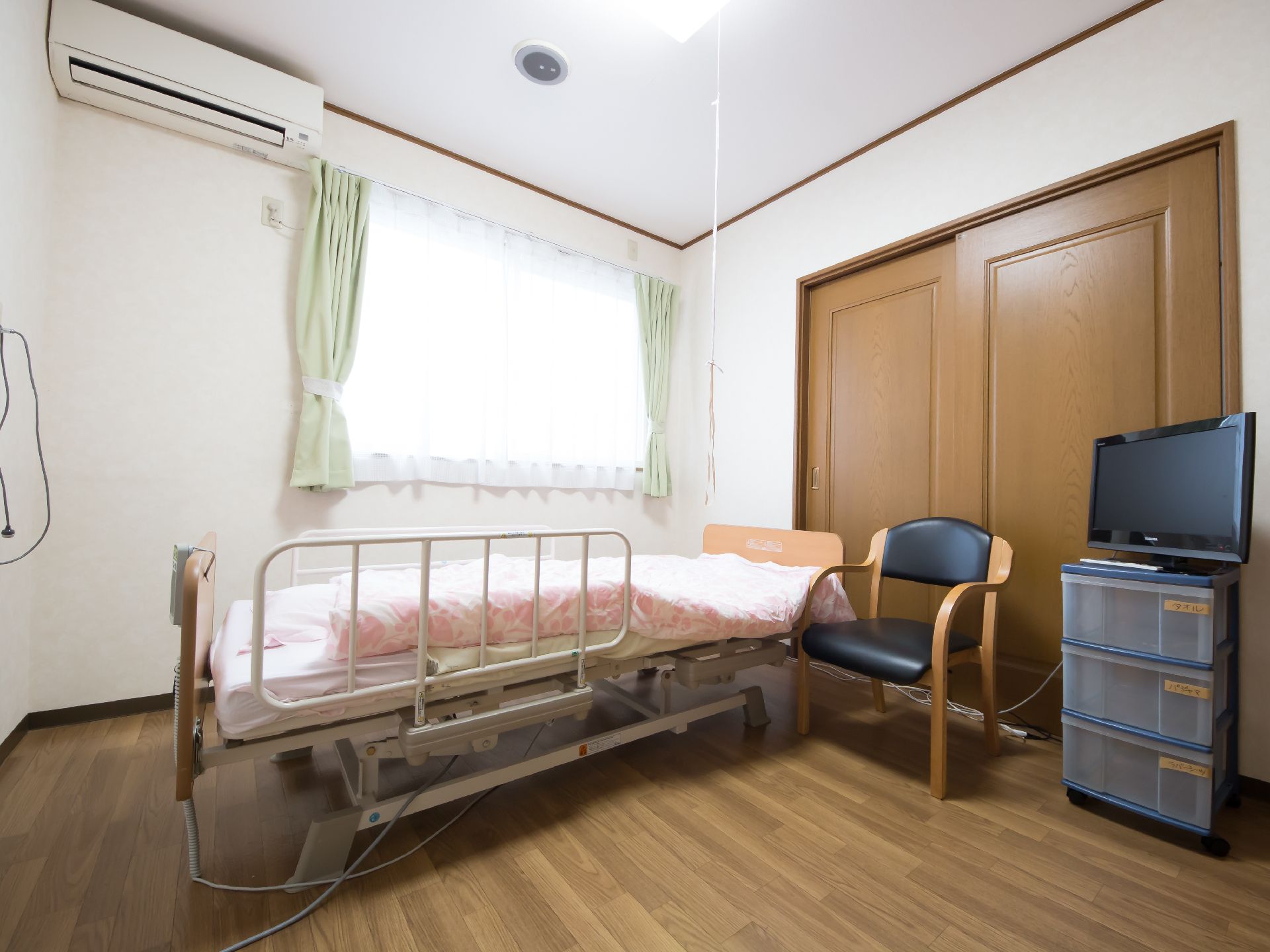 部屋の中央に電動ベッドと椅子、タンス、テレビがある部屋
