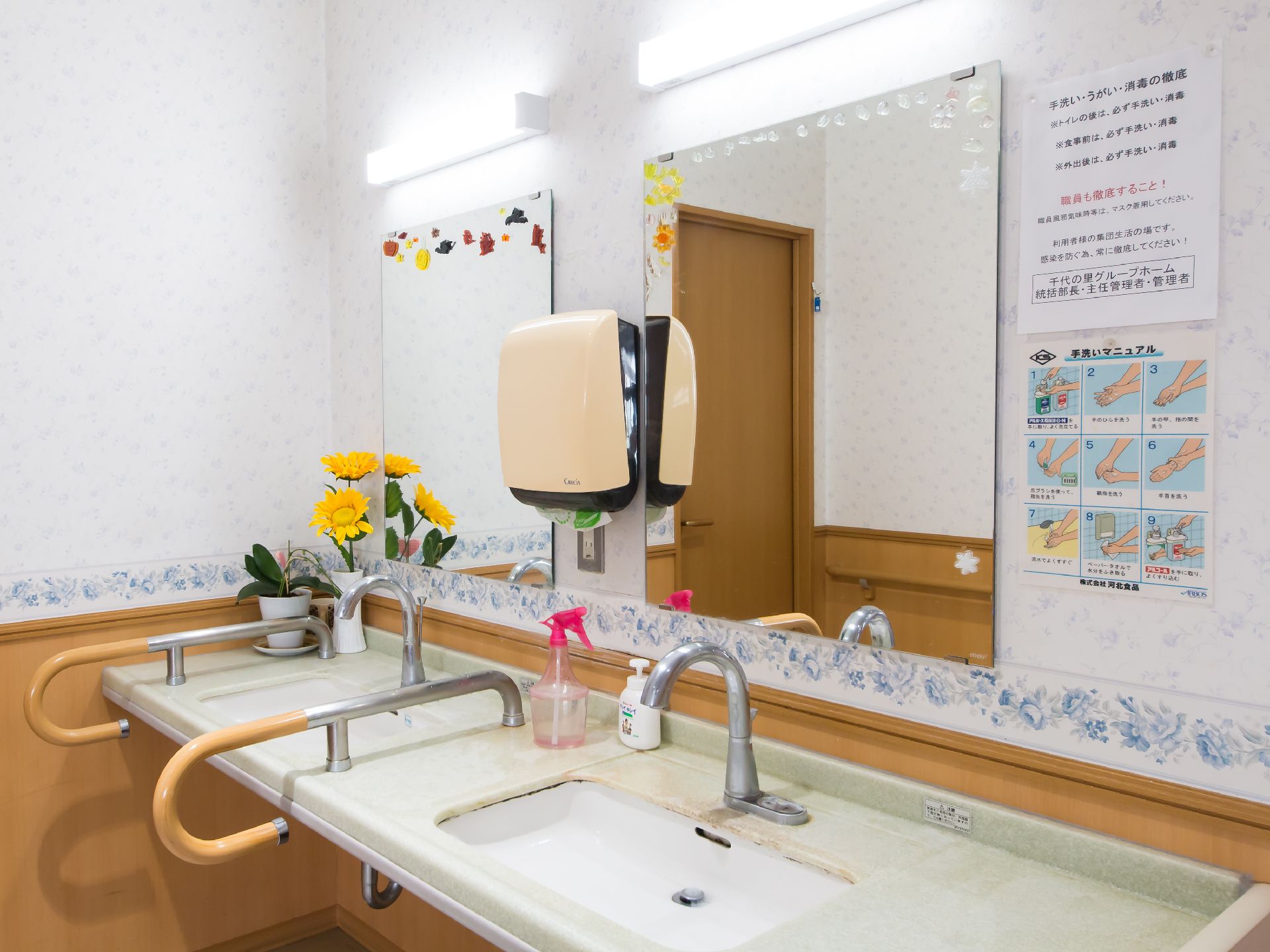 花が飾られている、二つ並んだ鏡と手すりがある洗面台