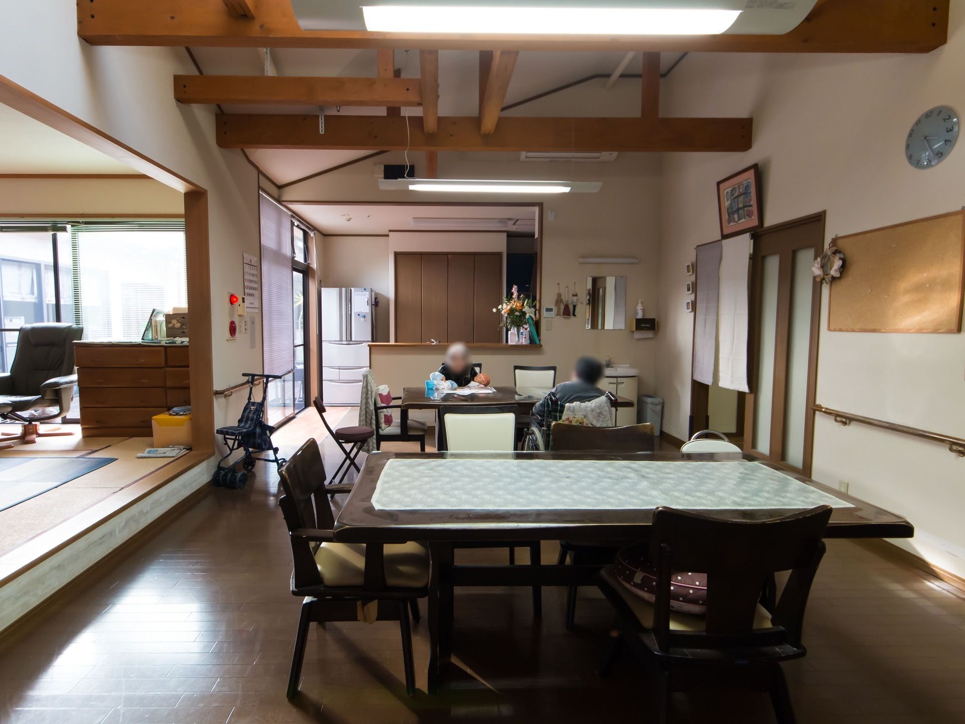 キッチンと和室が併設されている広い共有スペース。ダイニングテーブルと椅子などが並べられていて、テーブル席に座っている人が複数いるのが見える。
