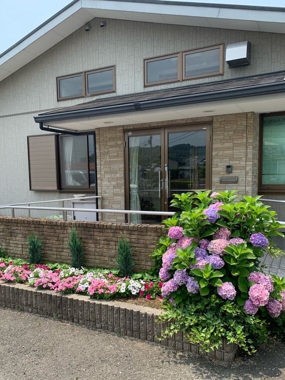 三角屋根の平屋建ての建物。周辺には色鮮やかなアジサイなど季節の花がたくさん咲いている。